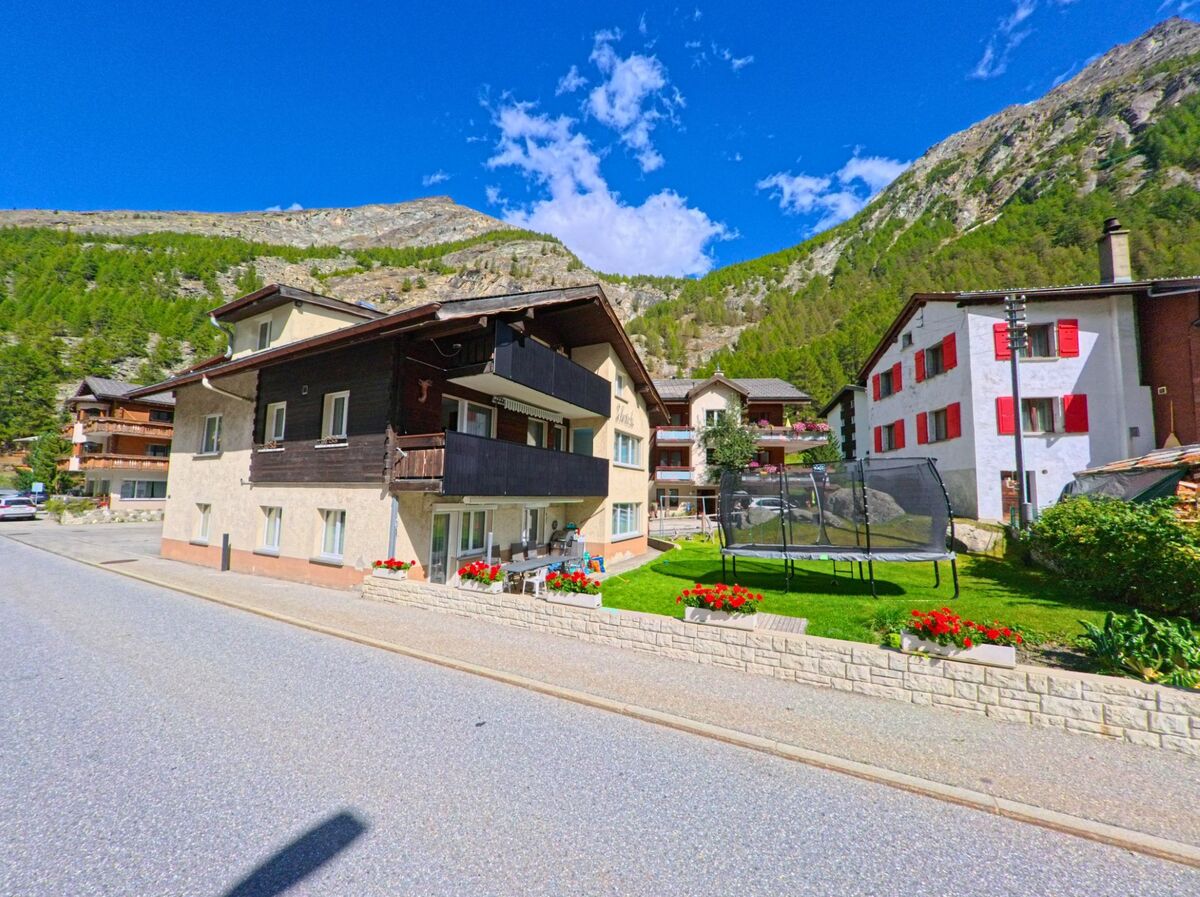 Ein Wohnhaus mit Balkonen und gepflegtem Garten mit Trampolin steht in Saas-Almagell (3905, Kanton Wallis) vor der Bergkulisse.