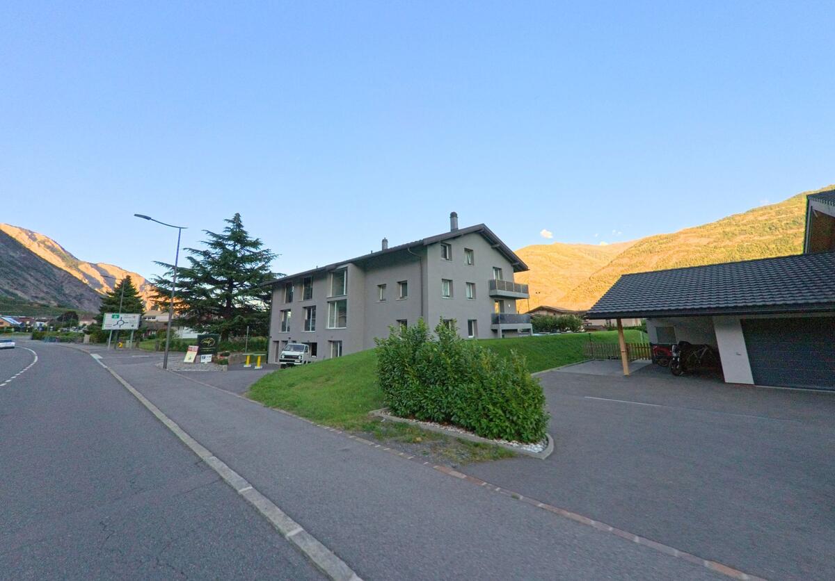 Ein Mehrfamilienhaus in Saillon (1913, Kanton Wallis) liegt an der Hauptstrasse mit Blick auf die sonnenbeschienenen Berghaenge.