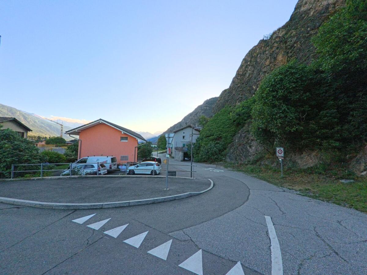 Eine enge Strasse fuehrt in Saillon (1913, Kanton Wallis) zwischen einem Wohnhaus und steilen Felsen weiter ins Tal.