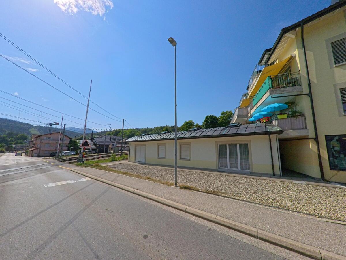 In Saint-Cergue (1264, Kanton Waadt) arbeitet ein Kammerjaeger an einem Wohnhaus mit bunten Sonnenschirmen auf den Balkonen nahe der Bahnlinie.
