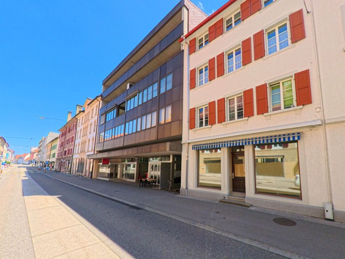 In einer Strasse von Saint-Imier (2610, Kanton Bern) stehen Wohn- und Geschaeftshaeuser in unterschiedlichen Baustilen, darunter ein modernes Gebaeude mit grossen Fenstern.