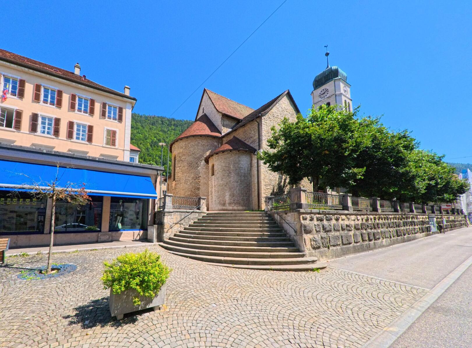 Vor der historischen Kirche in Saint-Imier (2610, Kanton Bern) führt eine breite Steintreppe von einem gepflasterten Platz mit Bänken und Pflanzkübeln hinauf.