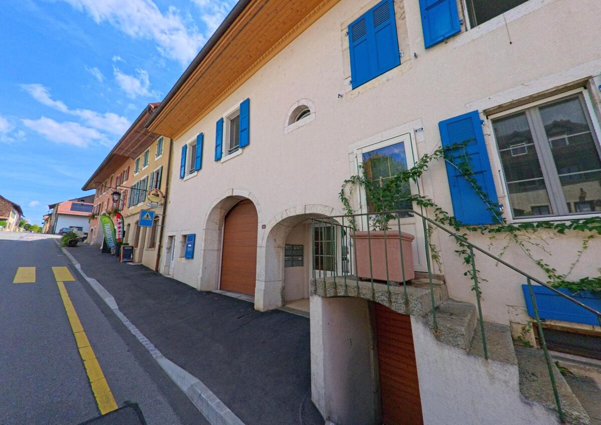 Entlang der Hauptstrasse in Saint-Livres (1176, Kanton Waadt) stehen Häuser mit bunten Fensterläden und kleinen Geschäften im Erdgeschoss.