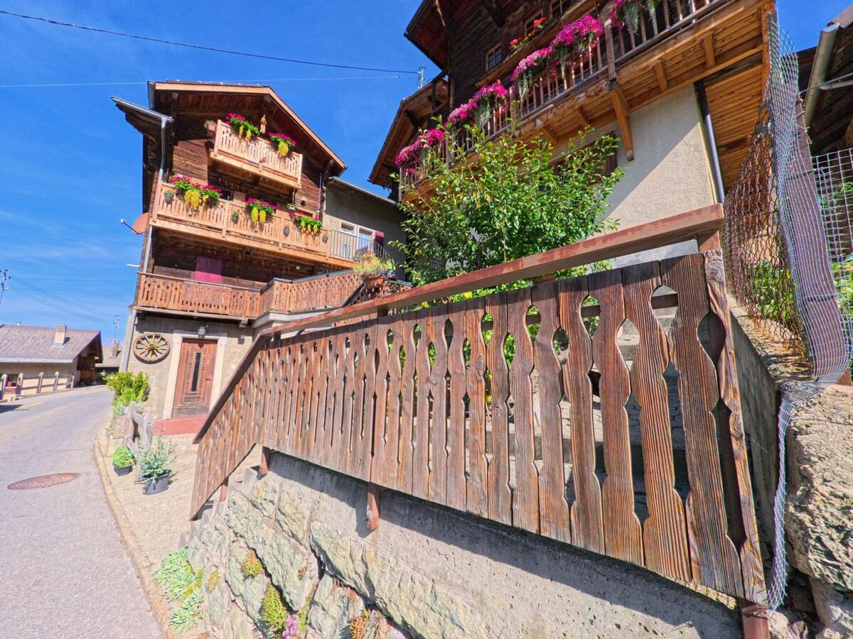 In Saint-Martin (1969, Kanton Wallis) stehen Holzhäuser mit reich geschmueckten Balkonen voller Blumen an einer schmalen Dorfstrasse.