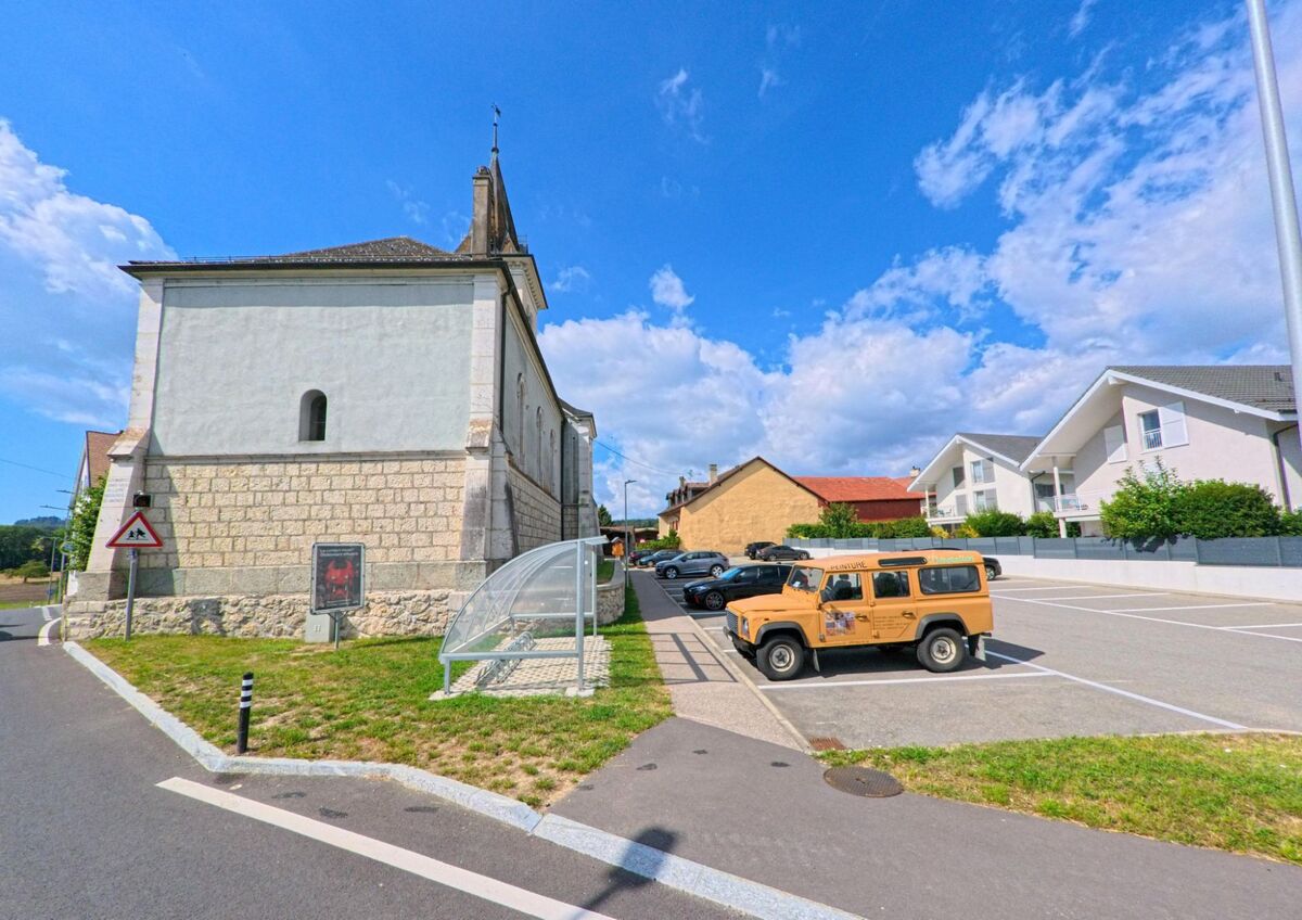 An der Kirche von Saint-Oyens (1187, Kanton Waadt) befindet sich ein Parkplatz mit mehreren Autos, darunter ein auffälliger gelber Geländewagen.