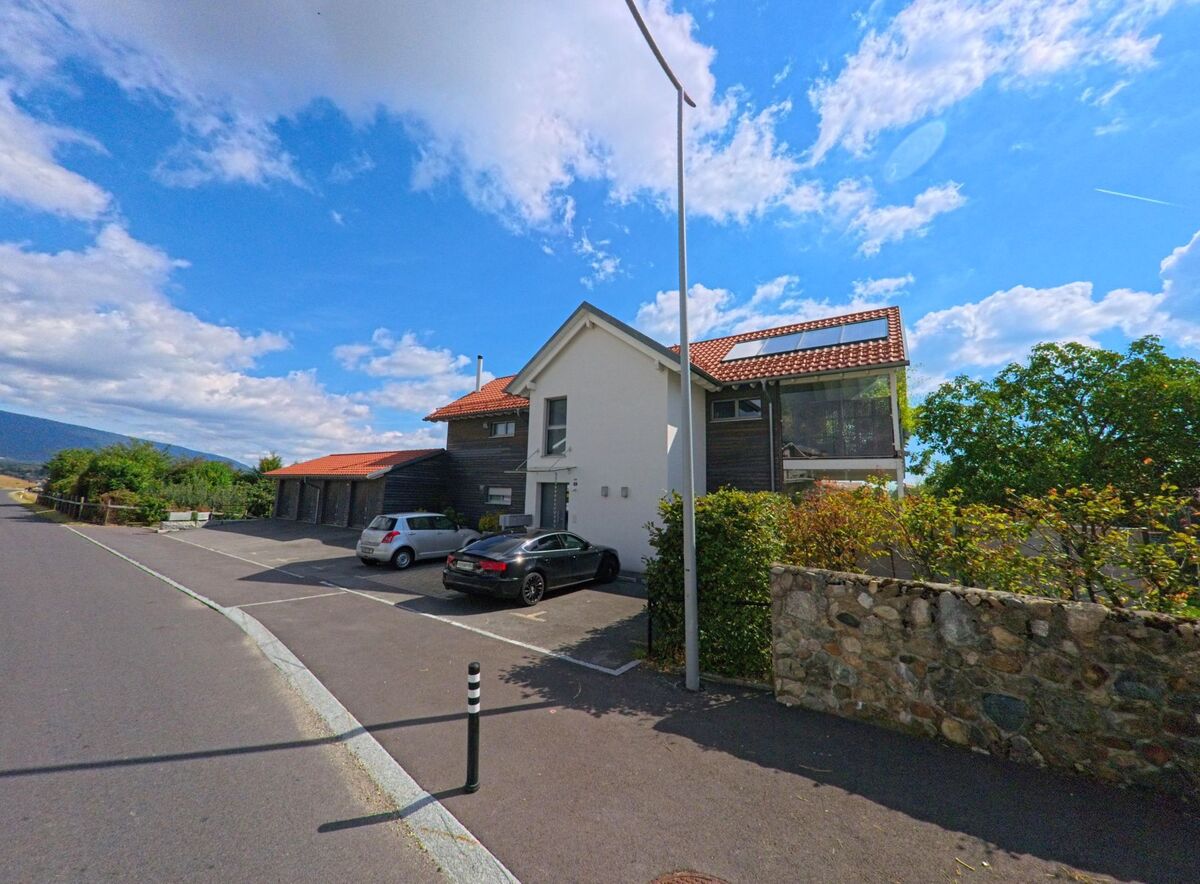 Ein modernes Wohnhaus mit Solarpanelen und Garagenplätzen steht in Saint-Oyens (1187, Kanton Waadt) an einer ruhigen Strasse mit Blick ins Tal.