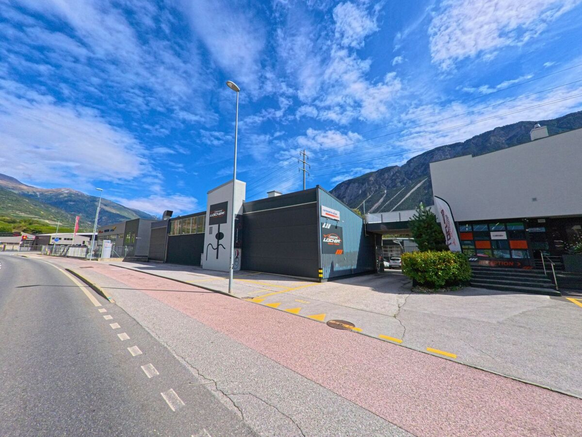 Ein modernes Industriegebaeude mit Beschriftungen steht an der Durchfahrtsstrasse von Salgesch (3970, Kanton Wallis) vor der Kulisse der Berge.