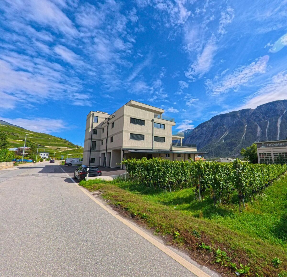 Ein modernes Wohnhaus in Salgesch (3970, Kanton Wallis) steht direkt neben einem Weinberg mit Blick auf die umliegenden Berge.