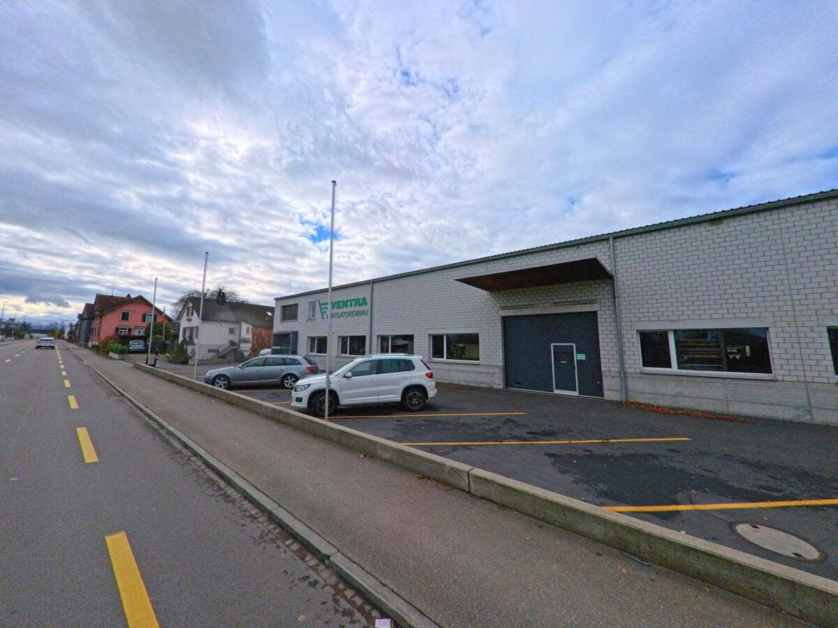 Ein eingeschossiges Gewerbegebäude mit Parkplätzen liegt entlang einer Nebenstrasse in Salmsach (8599, Kanton Thurgau) bei ruhiger Verkehrssituation.