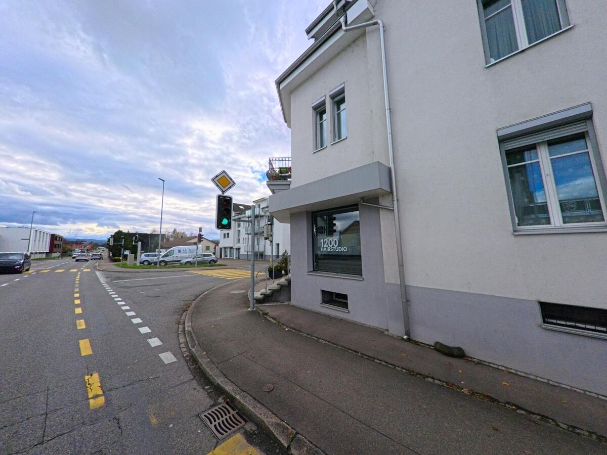An einer Kreuzung mit Ampel und Gehweg steht ein Wohn- und Geschäftsgebäude in Salmsach (8599, Kanton Thurgau) bei ruhigem Alltagsverkehr.