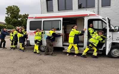 Mitglieder des Samaritervereins Pfäffikon ZH und Umgebung aus Pfäffikon (8330, Kanton Zürich) posieren in gelber Einsatzkleidung gemeinsam an einem Samariterfahrzeug.