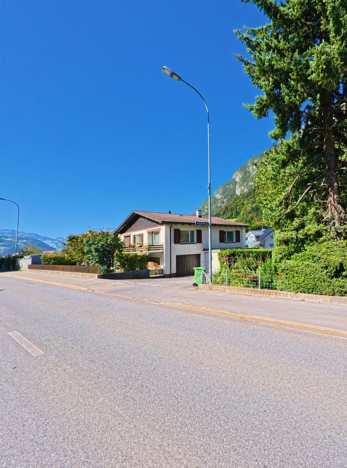 Ein Einfamilienhaus in Sargans (7320, Kanton St. Gallen) liegt an einer ruhigen Strasse mit Blick auf bewaldete Berghaenge im Hintergrund.