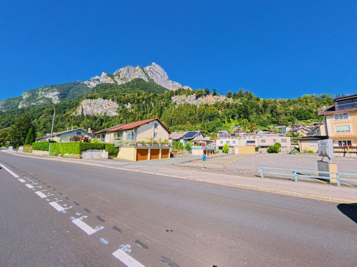 Am Ortsrand von Sargans (7320, Kanton St. Gallen) reihen sich Wohnhaeuser vor einer steilen bewaldeten Felswand unter klarem Himmel.