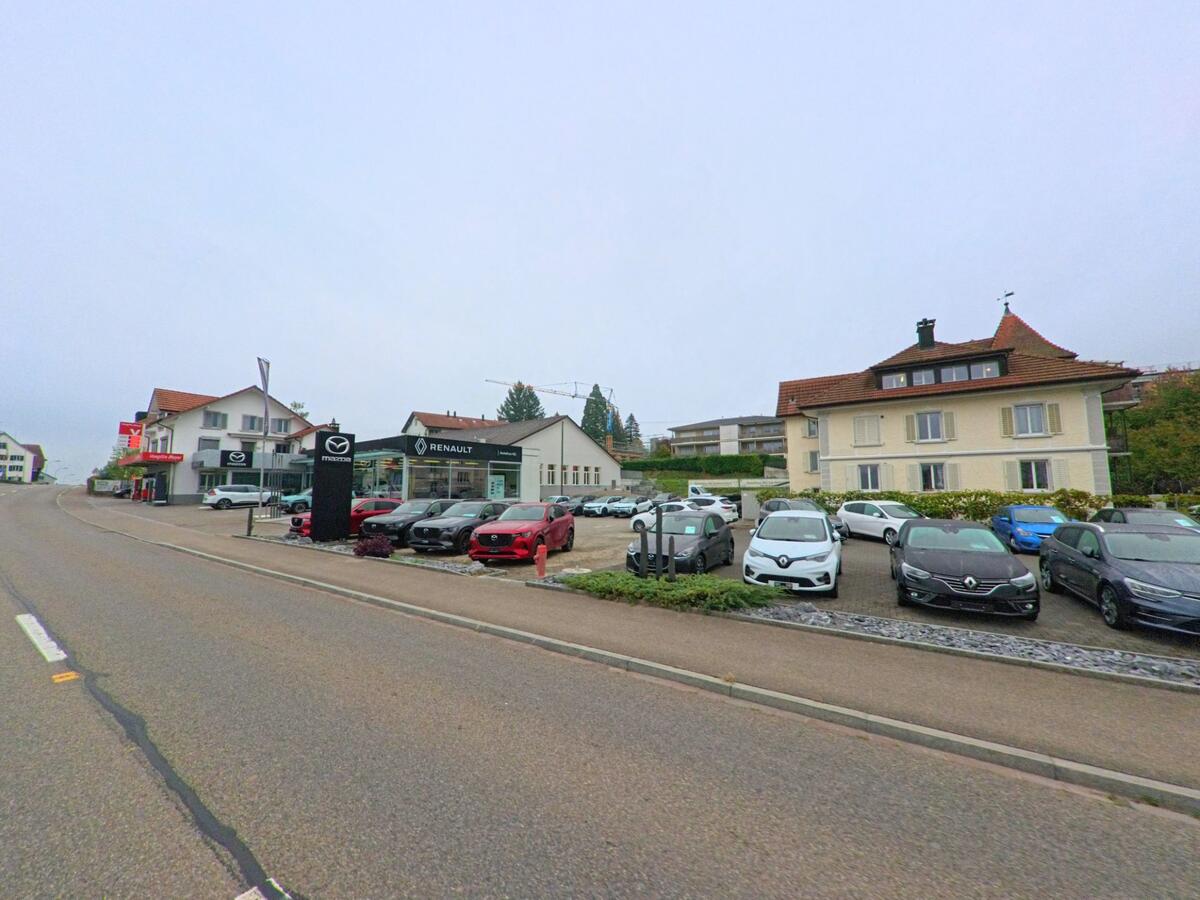 Ein Autohaus mit Ausstellungsplatz liegt an der Durchgangsstrasse von Sarmenstorf (5614, Kanton Aargau), wo zahlreiche Fahrzeuge vor Wohn- und Geschäftshäusern präsentiert werden.
