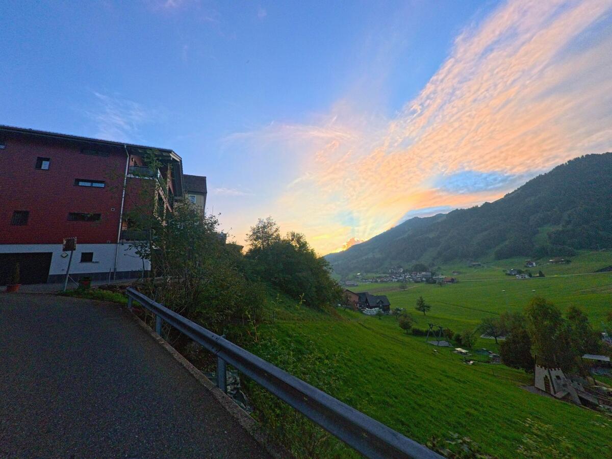 Von einer Leitplanke aus öffnet sich der Blick ins Tal bei Abendlicht in Sattel (6417, Kanton Schwyz).