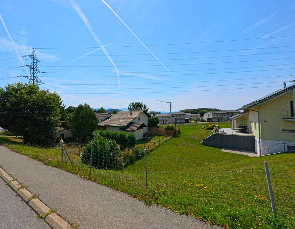 Von einem Gehweg in Savigny (1073, Kanton Waadt) blickt man auf Einfamilienhaeuser und Neubauten unter Stromleitungen.