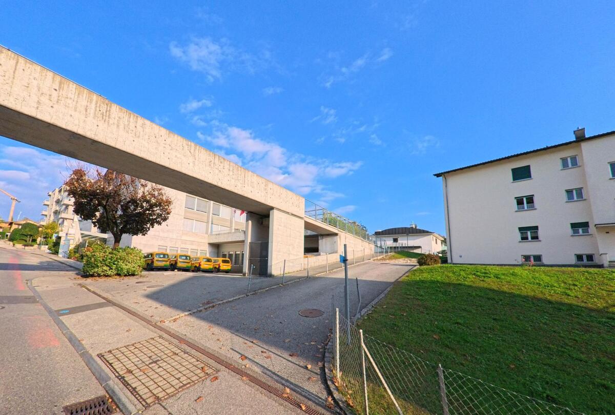 Neben einer markanten Betonüberdachung verläuft in Savosa (6942, Kanton Tessin) eine Zufahrtsstrasse zu öffentlichen Gebäuden und angrenzenden Grünflächen.