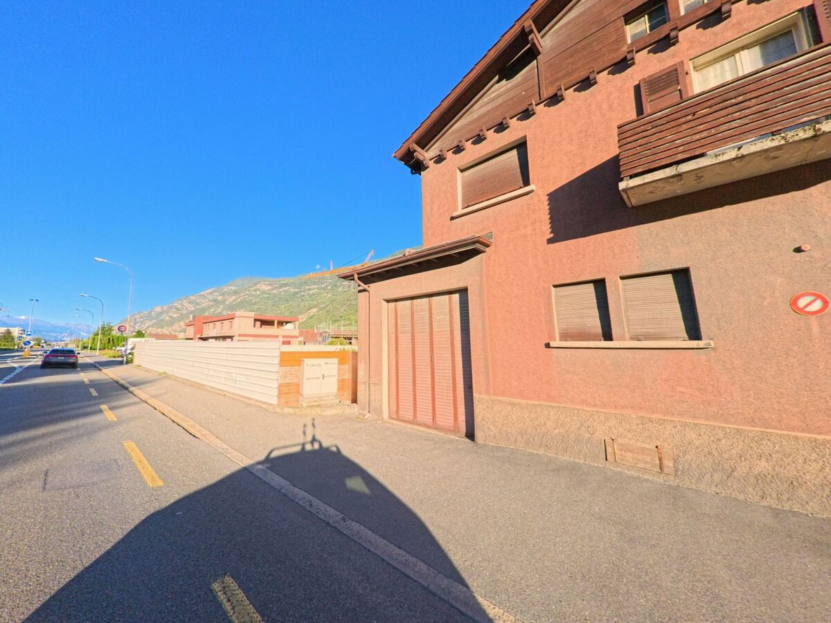 Ein Wohnhaus mit geschlossenen Fensterlaeden steht in Saxon (1907, Kanton Wallis) direkt an einer Strasse mit Gehweg.