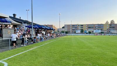 In Emmen (6032, Kanton Luzern) verfolgen zahlreiche Zuschauer ein Fussballspiel am Rand eines gepflegten Rasens, waehrend sich die Mannschaften auf dem Spielfeld bewegen.