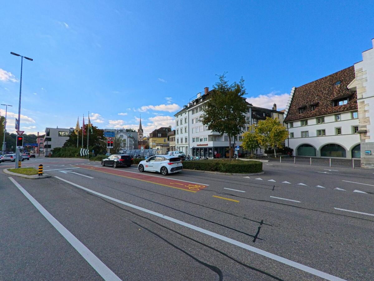 An einer verkehrsreichen Kreuzung mit Ampeln, Tramgleisen und Blick auf historische Gebaeude zeigt sich ein zentraler Stadtbereich von Schaffhausen (8200, Kanton Schaffhausen) bei klarem Himmel.