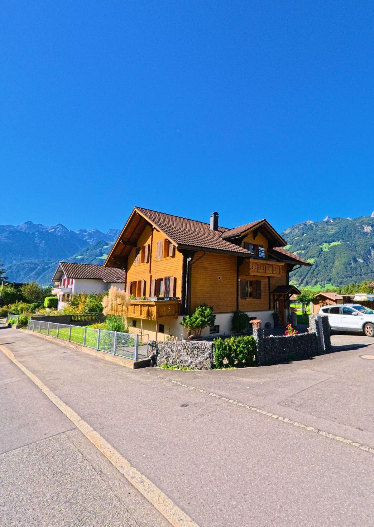 Ein traditionelles Holzhaus mit gepflegtem Garten steht in Schattdorf (6467, Kanton Uri) vor der Kulisse der umliegenden Alpen.