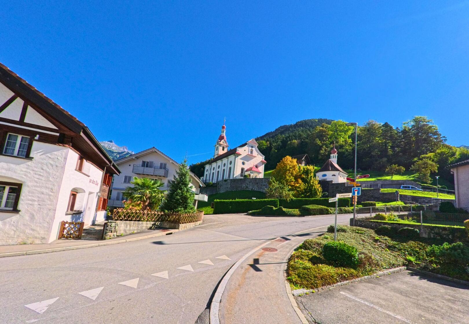 Die Pfarrkirche St. Josef erhebt sich in Schattdorf (6467, Kanton Uri) über den Häusern am Hang unter einem klaren blauen Himmel.