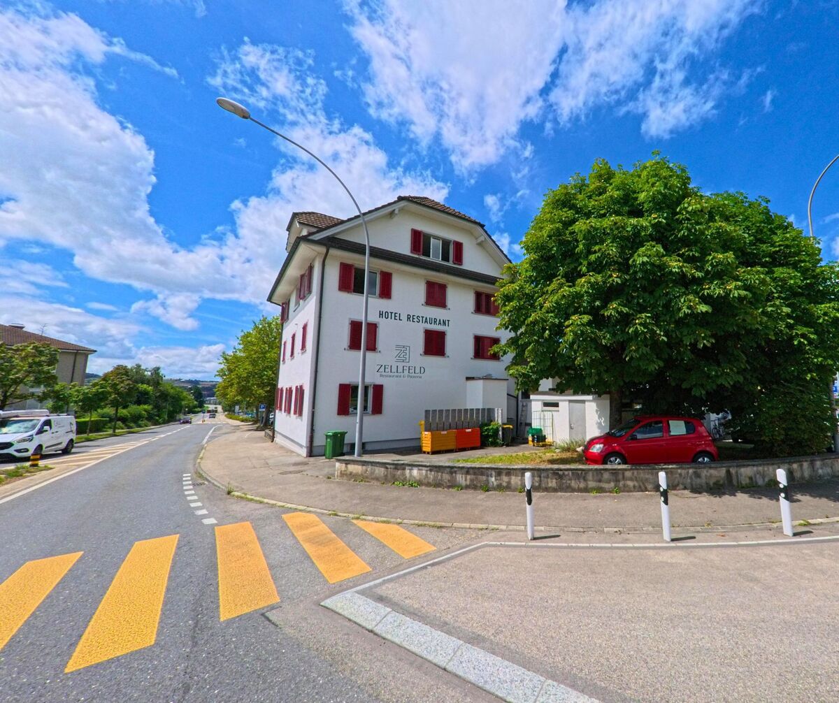 In Schenkon (6214, Kanton Luzern) steht an einer Kreuzung das Hotel Restaurant Zellfeld mit markanten roten Fensterläden und einem grossen Baum daneben.