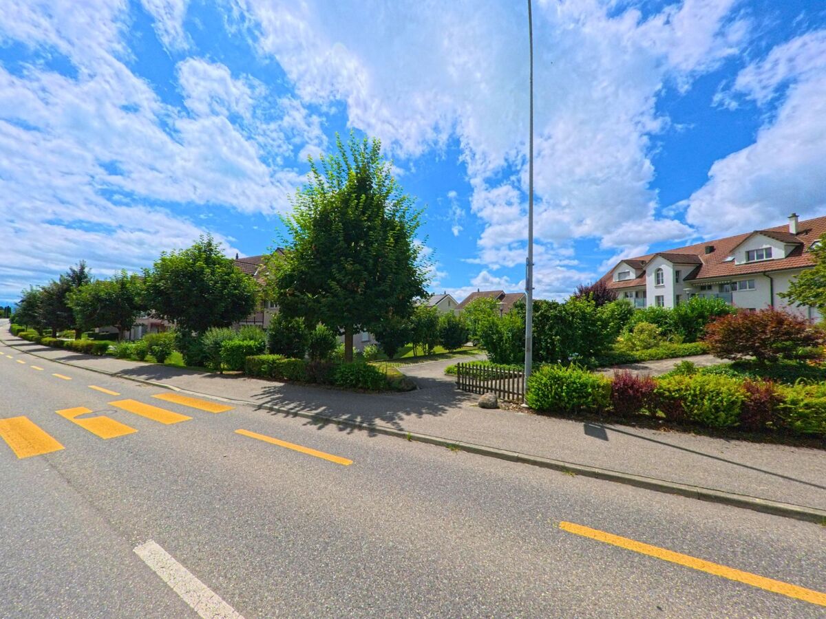In einem ruhigen Wohnviertel von Schenkon (6214, Kanton Luzern) verlaufen gepflegte Gärten und Bäume entlang einer verkehrsarmen Strasse mit Fussgängerstreifen.
