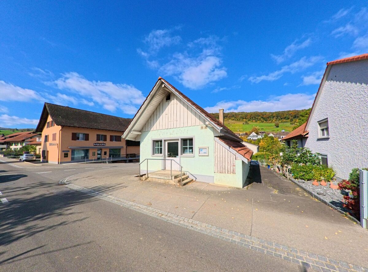 In Schinznach (5108, Kanton Aargau) stehen kleine Wohnhäuser mit Blick auf die umliegenden Rebberge, im Vordergrund verläuft eine ruhige Quartierstrasse.