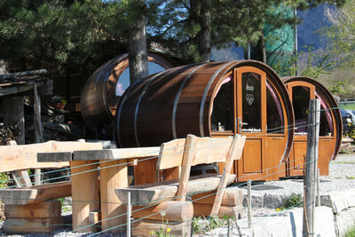 In Maienfeld (7304, Kanton Graubuenden) stehen die runden Holzfass-Unterkuenfte von SCHLAF-FASS neben rustikalen Sitzbaenken im Freien.