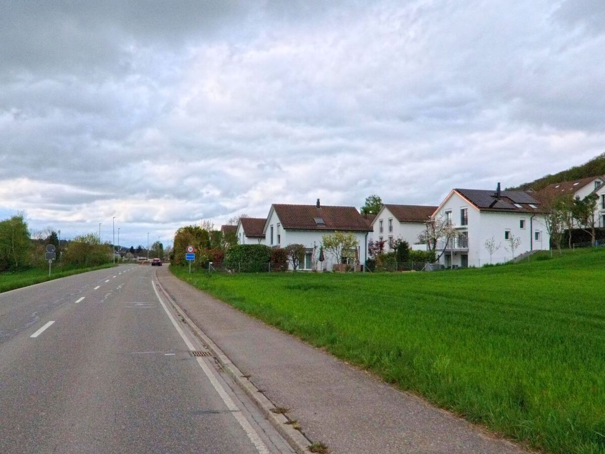 Moderne Einfamilienhaeuser mit Garten grenzen in Schleinikon (8165, Kanton Zürich) direkt an eine Landstrasse, die ins Dorf fuehrt.