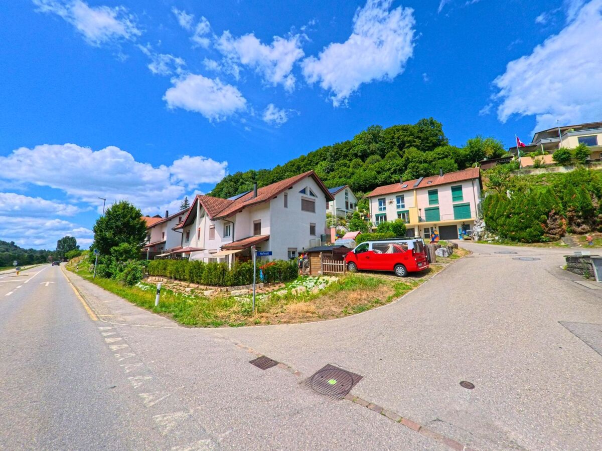 In Schlossrued (5044, Kanton Aargau) zweigt eine Nebenstrasse mit Wohnhaeusern in Hanglage von der Hauptstrasse ab, wobei bunte Fassaden und Gaerten das Ortsbild praegen.