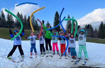 Auf einer verschneiten Wiese in Rapperswil Jona (8645, Kanton St.Gallen) stehen Kinder der Schneesport Schule Rapperswil Jona mit Skiern und bunten Schaumstoffstangen.