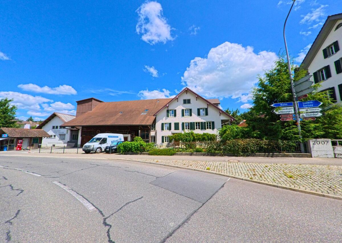 An einer Strassenkreuzung in Schoeftland (5040, Kanton Aargau) steht ein Wohnhaus mit angebautem Scheunentrakt und ein Wegweiser zeigt in verschiedene Richtungen wie Schlossrued und Luzern.
