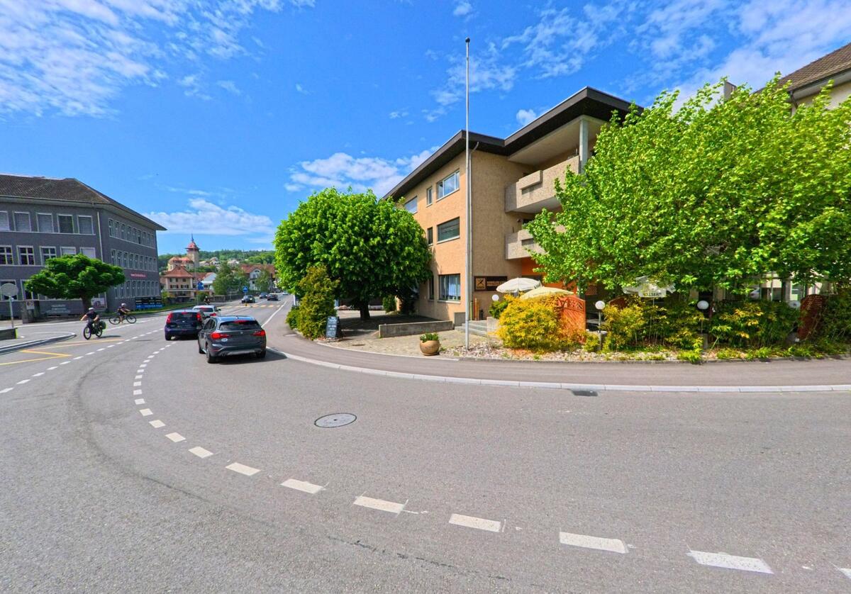 Eine Strassenkurve in Schönenwerd (5012, Kanton Solothurn) wird von Wohn- und Geschäftsgebäuden gesäumt, im Hintergrund ist der Kirchturm sichtbar.