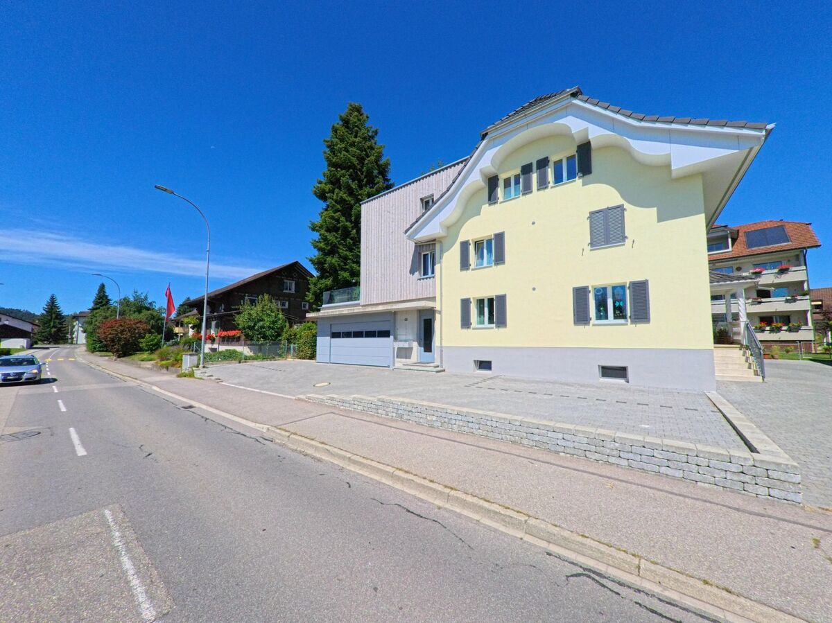 Ein hellgelbes Wohnhaus mit geschwungenem Giebel und moderner Garageneinfahrt steht in Schoetz (6247, Kanton Luzern) an einer ruhig gelegenen Nebenstrasse mit Einzelhaeusern.