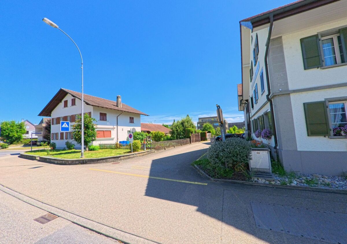 In Schoetz (6247, Kanton Luzern) markiert ein Fussgaengerschild die Kreuzung zweier Quartierstrassen, gesaeumt von Wohnhaeusern mit Fensterlaeden und Blumenschmuck.