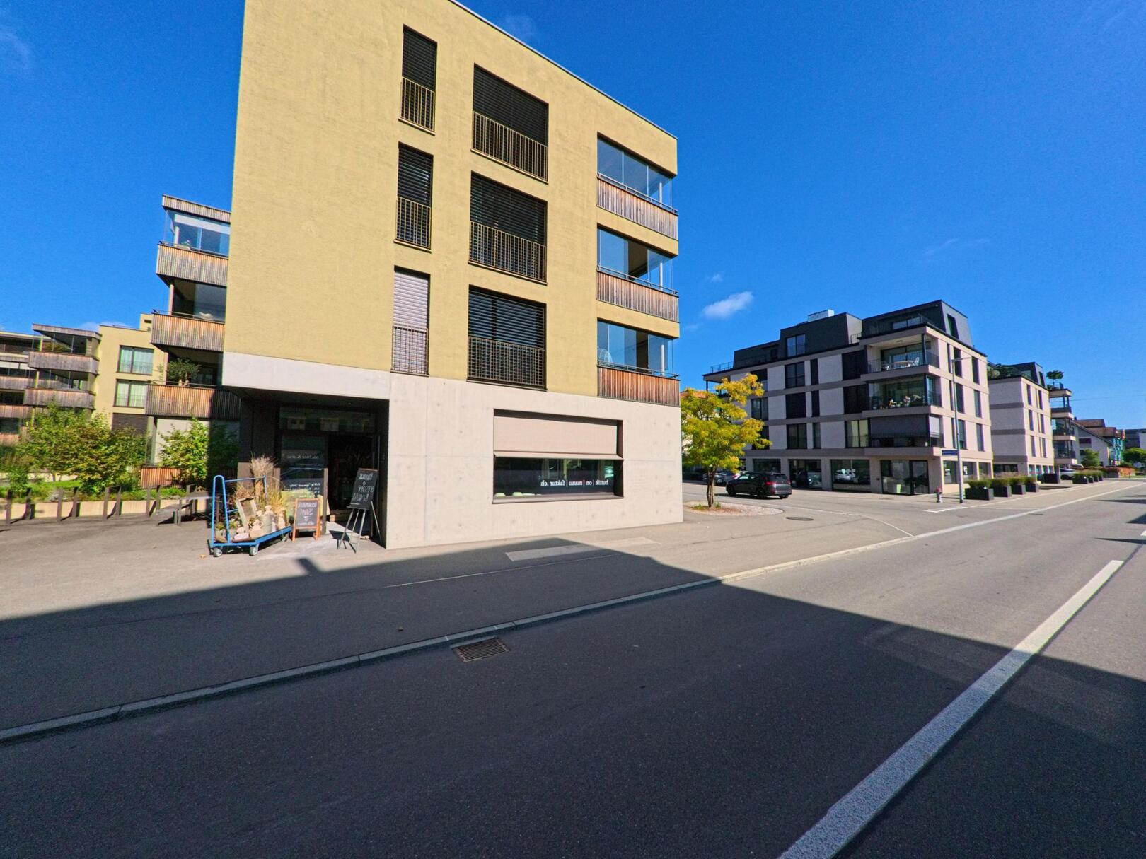 Vor modernen Wohnhaeusern in Schuebelbach (8862, Kanton Schwyz) verlaufen breite Strassen unter klarem Himmel an gepflegten Anlagen und Balkonen vorbei.