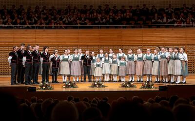 Der Schüler- und Jugendchor Utopia aus Escholzmatt-Marbach (6182, Kanton Luzern) steht in traditioneller Kleidung gemeinsam auf einer Bühne vor Publikum.