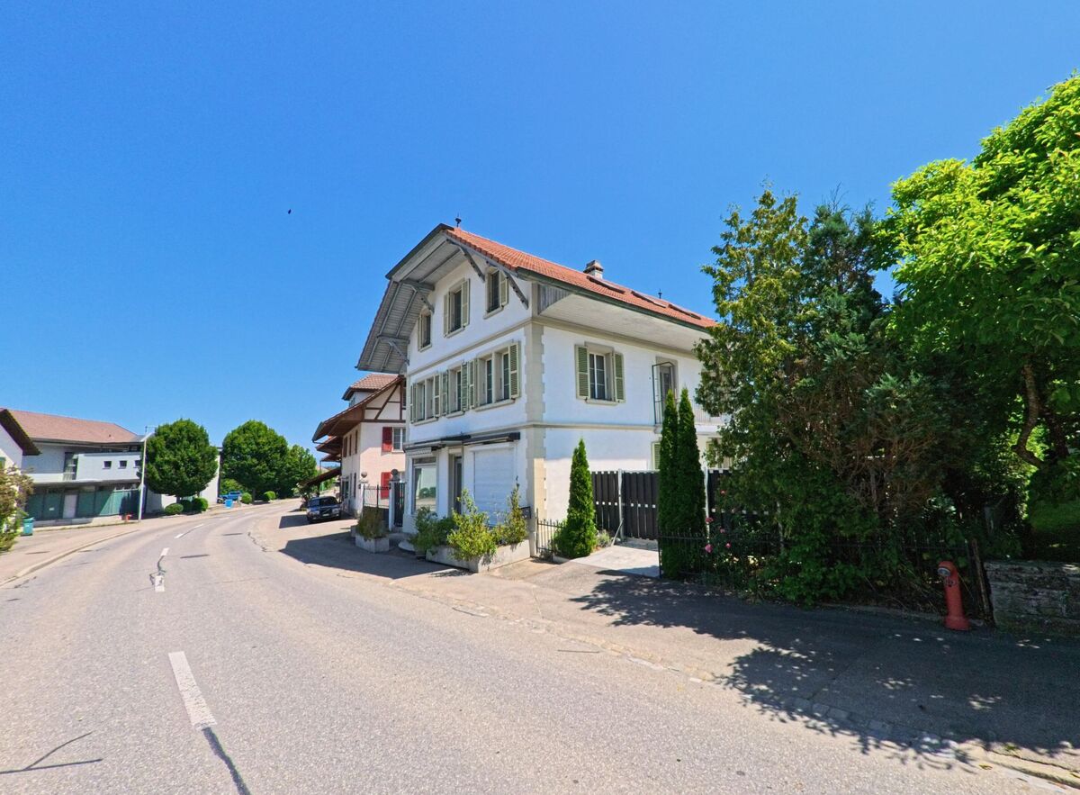 Ein charmantes Haus in Schüpfen (3054, Kanton Bern) steht am Straßenrand, umgeben von grünen Bäumen und einem gepflegten Garten.