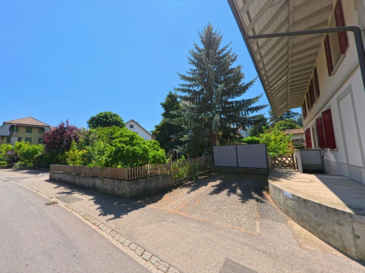Ein ruhiges Wohngebiet in Schüpfen (3054, Kanton Bern), mit einem gepflegten Garten und einem hohen Baum entlang der Straße.