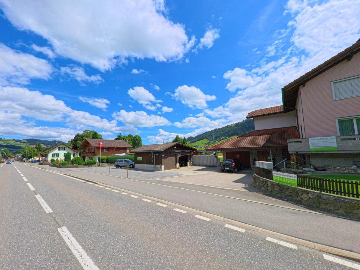 Am Ortsrand von Schüpfheim (6170, Kanton Luzern) reihen sich Einfamilienhäuser entlang einer breiten Strasse mit Blick auf bewaldete Hügel.