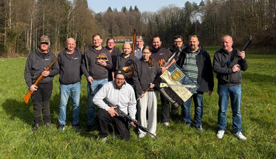 In Birmenstorf (5413, Kanton Aargau) posieren Mitglieder der Schützengesellschaft Birmenstorf mit Sportgewehren, Vereinsfahne und Auszeichnungen auf einer Wiese vor dem Schiessstand.