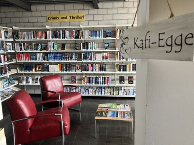 Zwischen roten Sesseln und gefuellten Buecherregalen zeigt diese Innenansicht einen Lesebereich der Bibliothek in Sumiswald (3454, Kanton Bern).