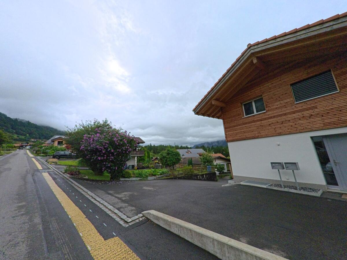 In Schwanden bei Brienz (3855, Kanton Bern) verläuft eine Wohnstrasse mit modernen Einfamilienhäusern und gepflegten Gärten mit blühenden Sträuchern.