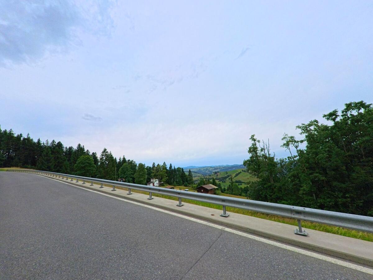 Eine Kurve der Landstrasse in Schwarzenberg (6013, Kanton Luzern) bietet einen weiten Ausblick über bewaldete Hügel und das Tal mit vereinzelten Häusern.