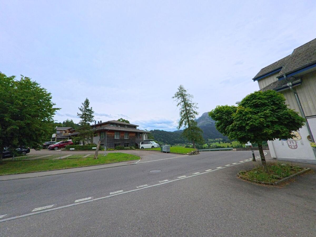 In Schwarzenberg (6013, Kanton Luzern) treffen mehrere Strassen an einem kleinen Platz mit Bäumen aufeinander, im Hintergrund erheben sich grüne Hügel und Berge.
