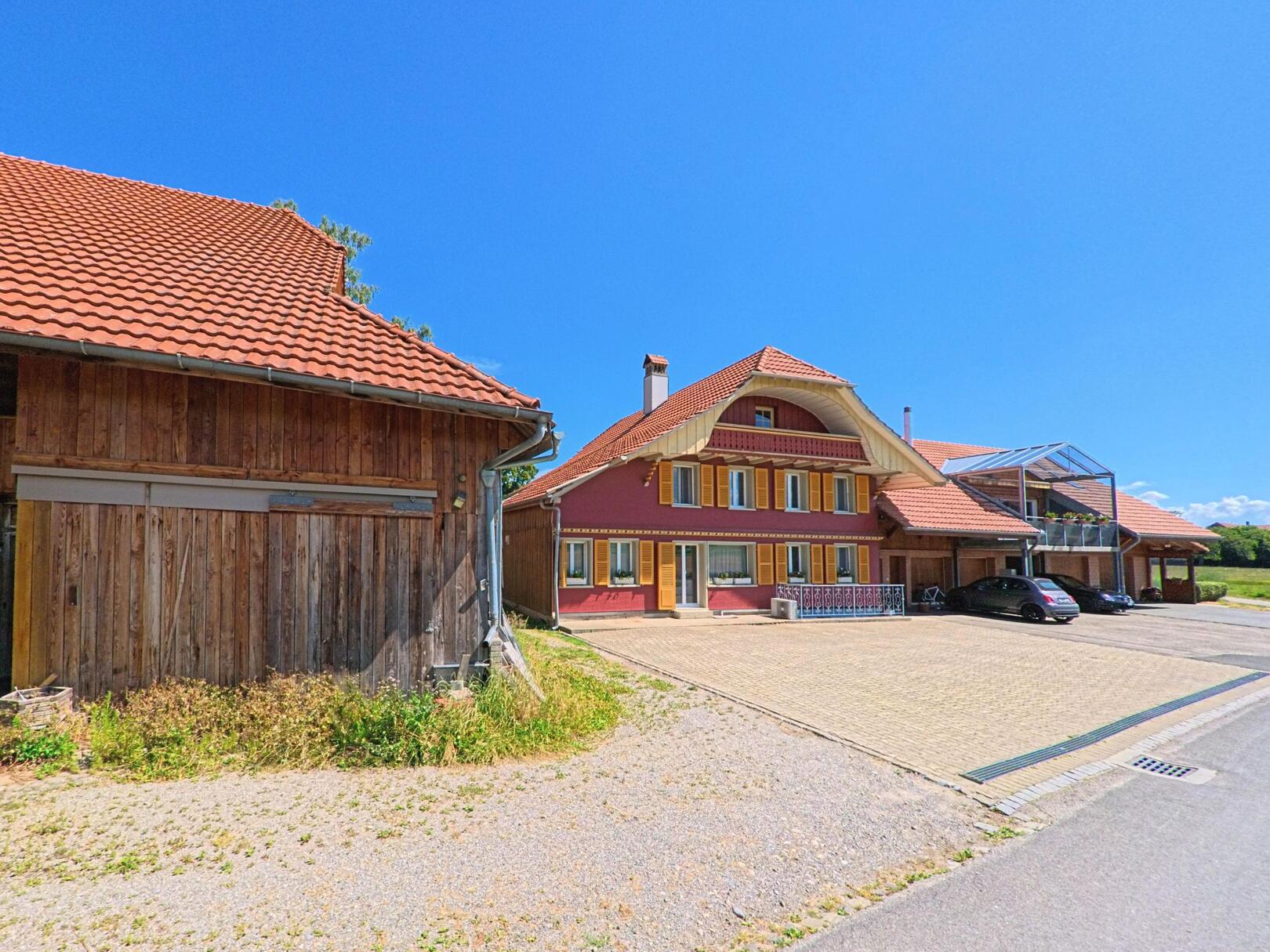In Schwarzenburg (3152, Kanton Bern) steht ein modernisiertes Bauernhaus mit rotem Anstrich und gelben Fensterläden neben einem Holzschopf an einer Nebenstrasse.