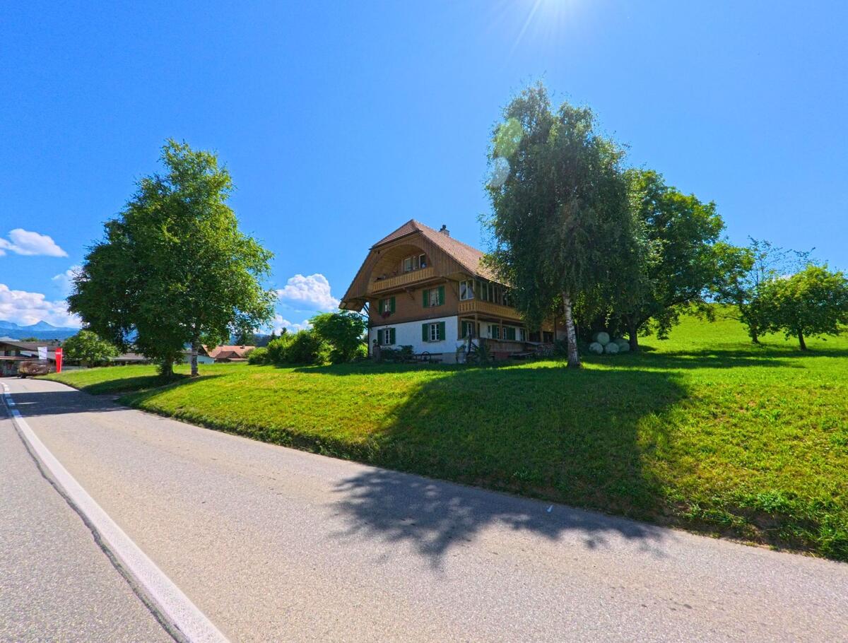 Auf einer kleinen Anhöhe in Schwarzenburg (PLZ 3152, Kanton Bern) steht ein traditionelles Wohnhaus mit grünem Fensterladen, umgeben von Bäumen und Wiesen.