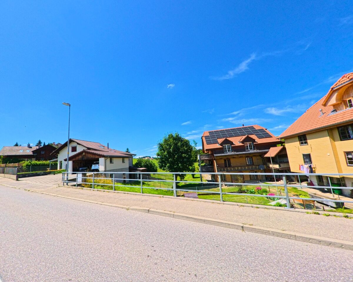 In einem Wohnquartier von Schwarzenburg (3152, Kanton Bern) stehen mehrere Einfamilienhäuser mit gepflegten Gärten und Solarpanels entlang einer leicht abfallenden Strasse.